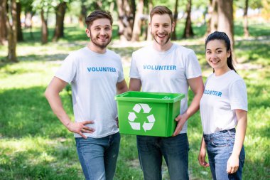 young volunteers with green recycling box standing in park  clipart