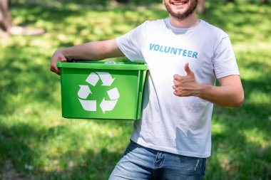 cropped view of man holding recycling box and showing thumb up clipart