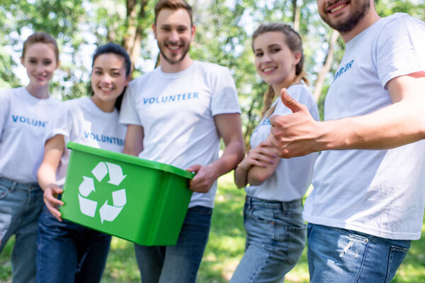 volunteers with green recycling box showing thumb up after cleaning park 