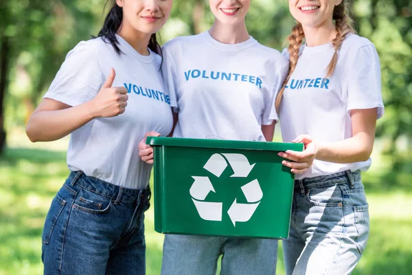 cropped view of young volunteers with green recycling box showing thumb up
