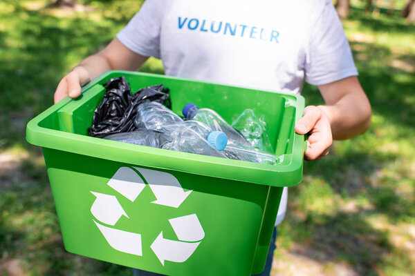 обрезанный вид волонтера, держащего коробку для переработки с пластиковым мусором
