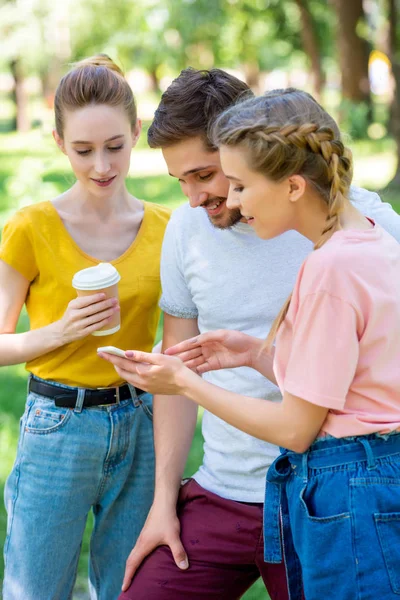 年轻的朋友用一次性咖啡杯使用智能手机在公园 — 免费的图库照片