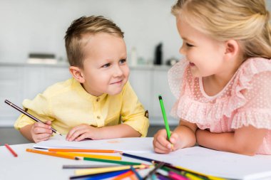 adorable kids smiling each other while drawing with colored pencils together clipart