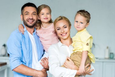iki sevimli çocukla birlikte evde kameraya gülümseyen mutlu aile 