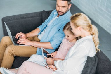 kanepede oturan ve dijital cihazlar kullanarak çocuk ailenin yüksek açılı görünüş  