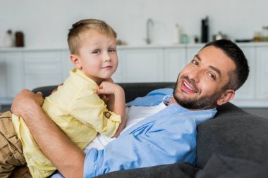 Babası koltukta yalan ve kameraya gülümseyen sevimli küçük oğlu ile