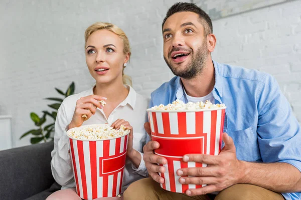 stock image excited couple eating popcorn and looking away at home