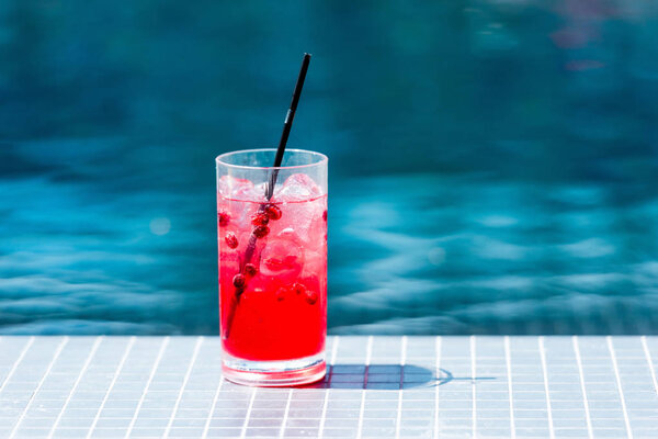 close-up shot of glass of red berry cocktail on poolside