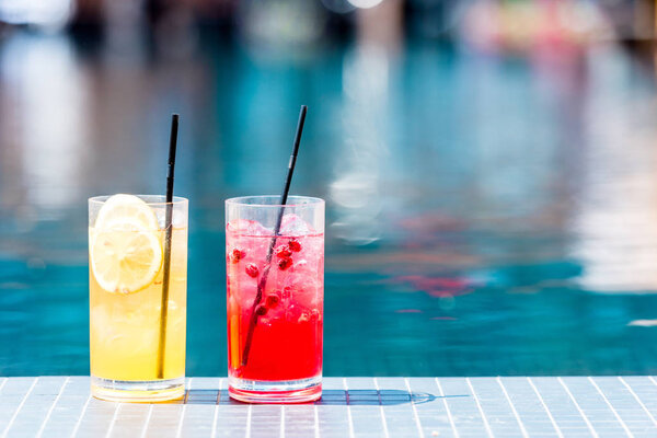 close-up shot of glasses of delicious red and orange cocktails on poolside