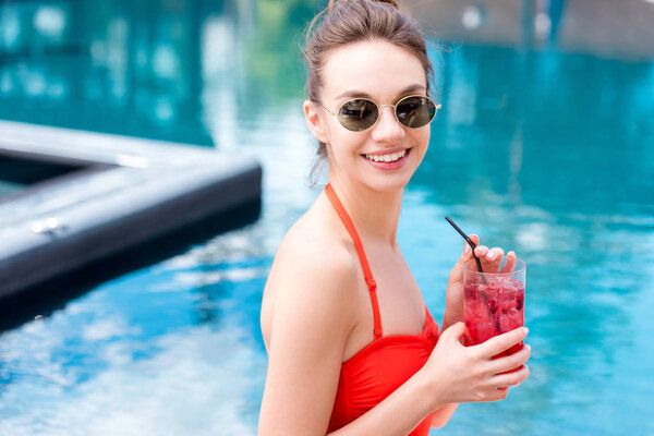happy young woman in vintage sunglasses with berry cocktail at poolside