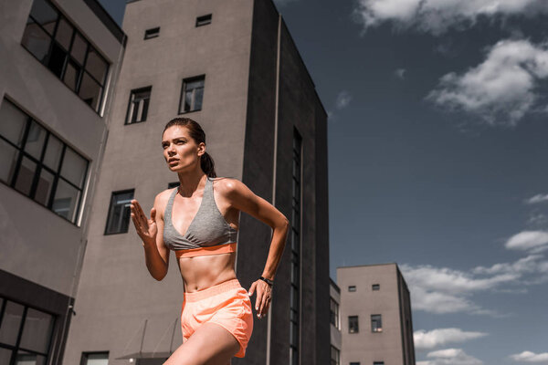 young concentrated sportswoman running with fitness tracker in city 