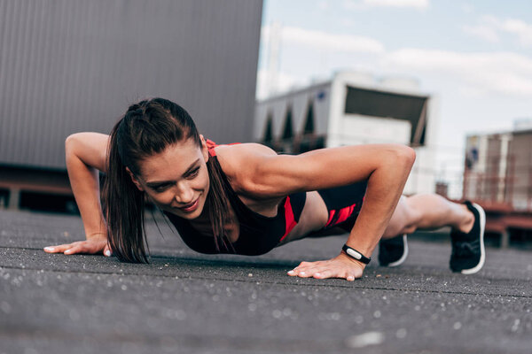 young smiling sportswoman doing push up on asphalt in city