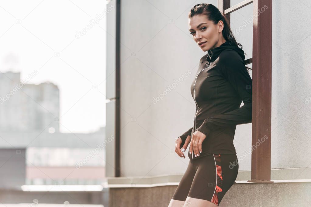 athletic woman posing in sportive thermal clothes near ladder on roof 