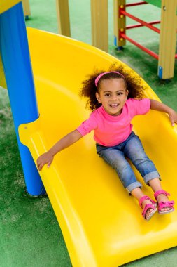  smiling curly african american little kid sliding down from hill at playground  clipart