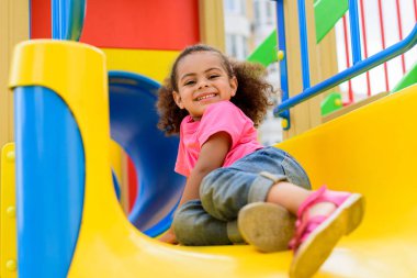 happy african american little kid sliding down from hill at playground  clipart