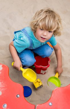 küçük çocuk plastik kaşık toz, kalıpları ve kum playgorund, kova ile oynarken yüksek açılı görünüş 