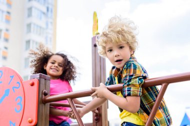 selective focus of two multiethnic little kids having fun at playground  clipart