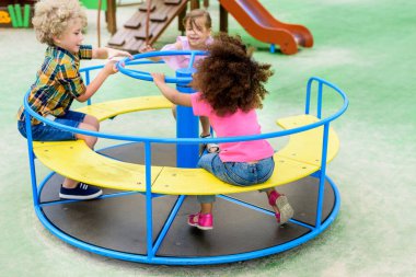 happy adorable little children riding on carousel at playground  clipart