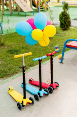 selective focus of three childish kick scooters with colorful air balloons at playground  clipart