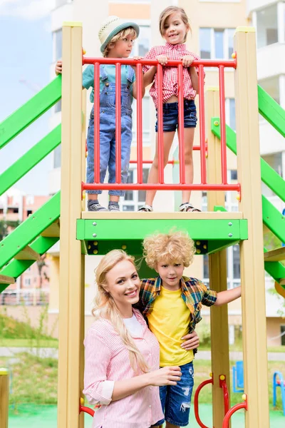 Mãe Feliz Abraçando Filho Enquanto Seu Irmão Irmã Atrás Playground — Fotografia de Stock