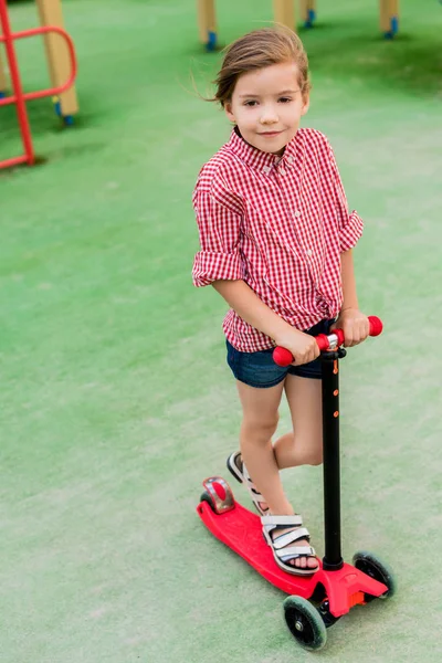 幸せな小さな子供の遊び場でのキック スクーターに乗って — ストック写真