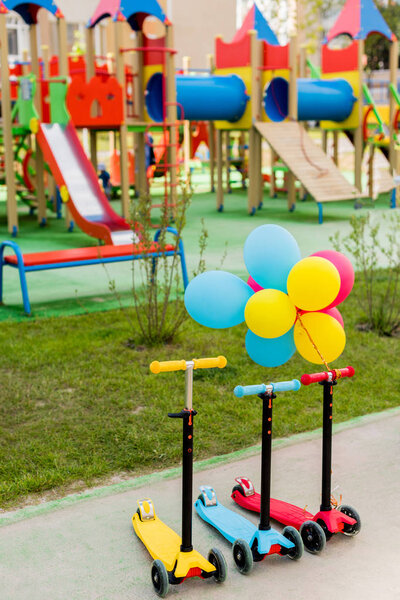 three childish kick scooters placed in row with colorful air balloons at playground 