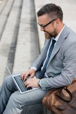 dizüstü bilgisayar kullanarak ve quay deri çanta ile oturan sakallı işadamı 
