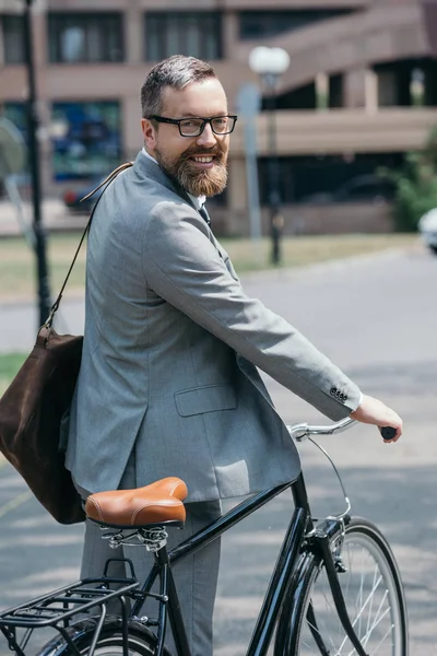 自転車の側に立って 市の路上カメラを見て笑顔のハンサムな実業家 — ストック写真