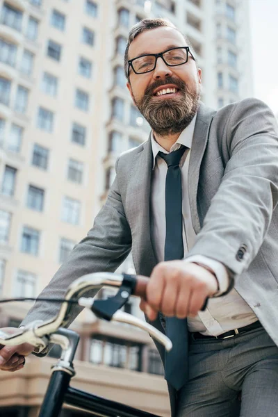 handsome smiling businessman riding bike in city
