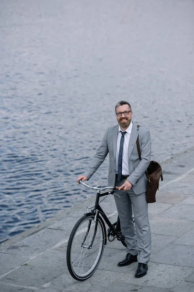 handsome businessman with leather bag standing on quay with bicycle