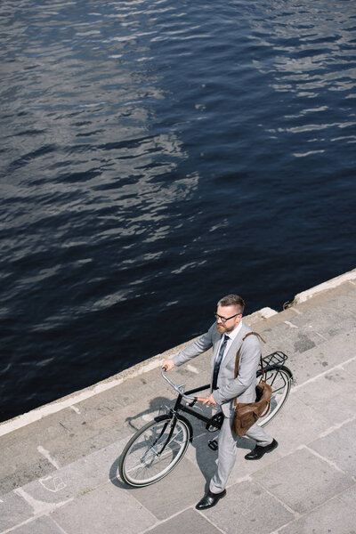 overhead view of handsome businessman walking with bicycle on quay near river