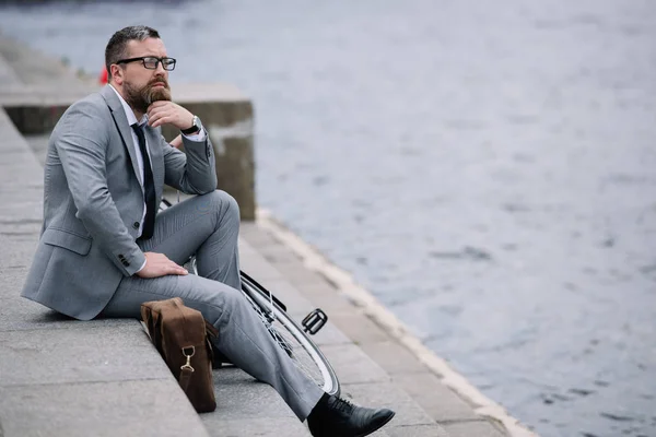 岸壁で階段に座っている灰色のスーツでハンサムな思いやりのある実業家 — ストック写真