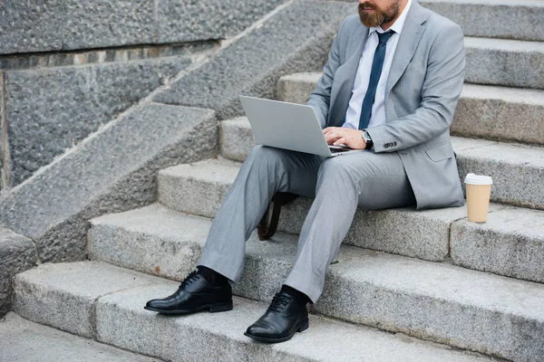 Tek kullanımlık dizüstü kullanarak ve merdivenlerde oturan kahve fincan ile işadamı ve kırpılmış görmek