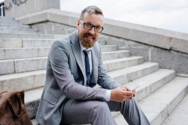 Smartphone kullanarak ve şehirde merdivenlerde oturan yakışıklı işadamı