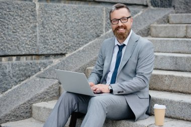 dizüstü bilgisayar kullanarak ve kahve ile merdivenlerde oturan işadamı