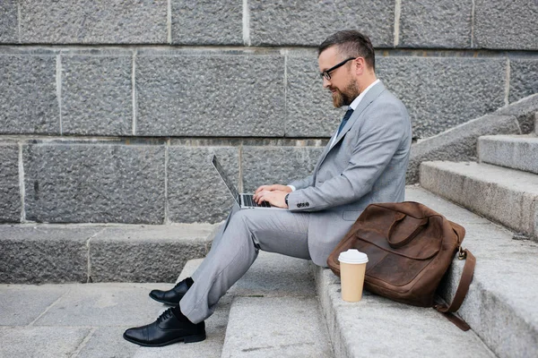 businessman with leather bag using laptop and sitting on stairs