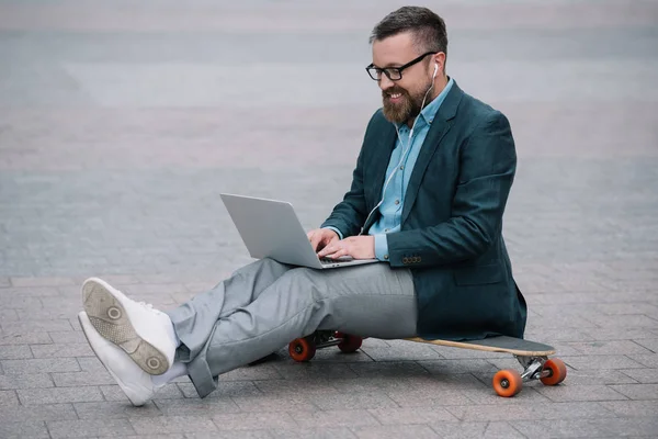 Stijlvolle Europese Man Met Behulp Van Laptop Zittend Het Skateboard — Stockfoto