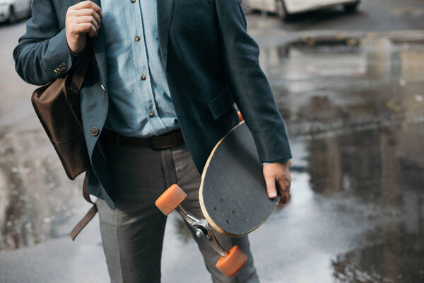 cropped view of stylish man with longboard walking in city