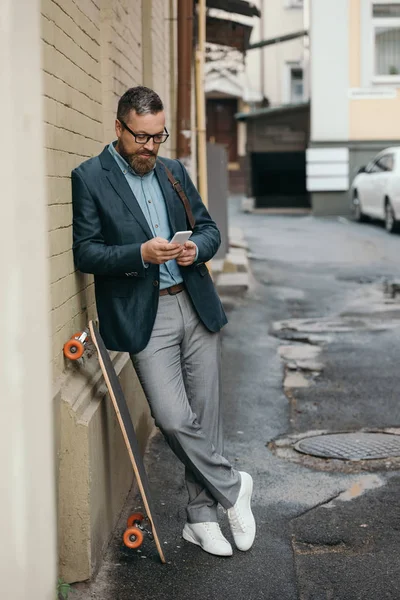 Bebaarde Man Met Longboard Gebruikend Smartphone Stad — Stockfoto