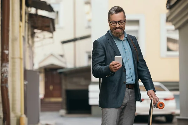 Stijlvolle Bebaarde Man Met Longboard Gebruikend Smartphone Stad — Stockfoto