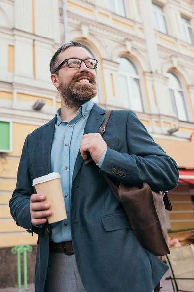 stylish smiling man with leather bag and disposable cup of coffee in city