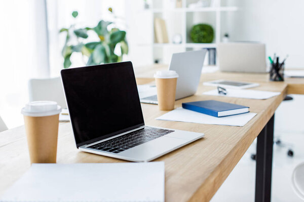 ноутбук с чистым экраном и одноразовые кофейные чашки на столе в офисе
