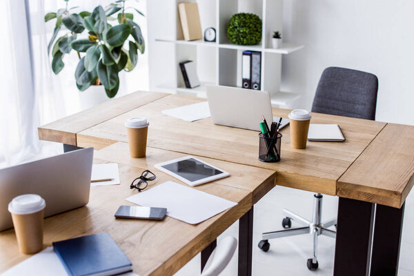 laptops, tablet and disposable coffee cups on tables in business office