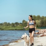 Atractivo joven asiático deportista corriendo con golden retriever cerca del mar