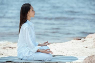 yoga mat deniz ardha padmasana (yarım lotus poz) içinde odaklı kadın yan görünüm 