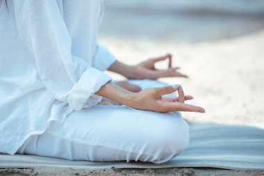 cropped image of woman in ardha padmasana (half lotus pose) on yoga mat by sea  clipart