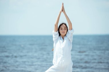 Asyalı kadın kapalı gözlerle asana vrikshasana (ağaç poz) deniz yoluyla sahilde duran 