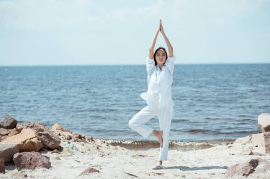 Asyalı kadın asana vrikshasana (ağaç poz) deniz yoluyla sahilde duran önden görünümü 