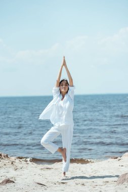 asana vrikshasana (ağaç poz) deniz yoluyla sahilde duran Genç Asyalı kadın 