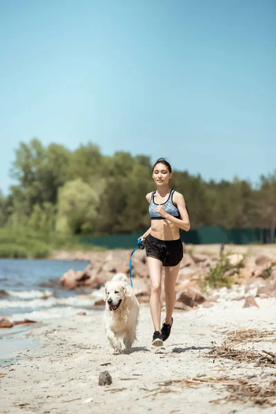 Női Sportoló Jogging Kutya Strandon Napközben — Stock Fotó